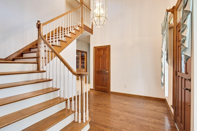 entrance foyer with a towering ceiling, a notable chandelier, baseboards, stairway, and wood finished floors