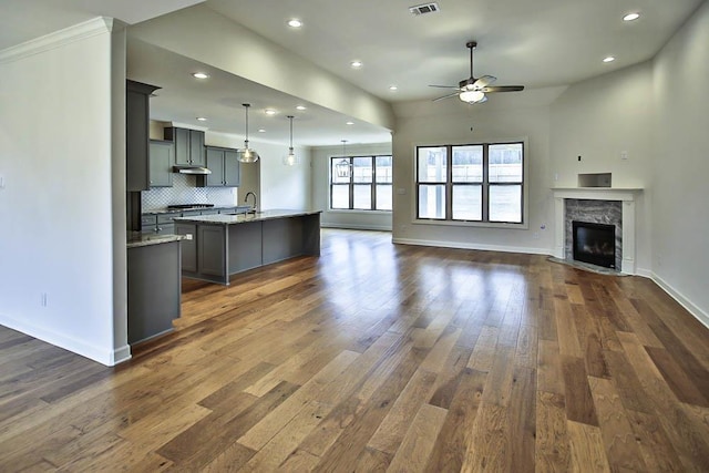 kitchen featuring pendant lighting, dark wood-type flooring, gray cabinets, a kitchen island with sink, and light stone counters