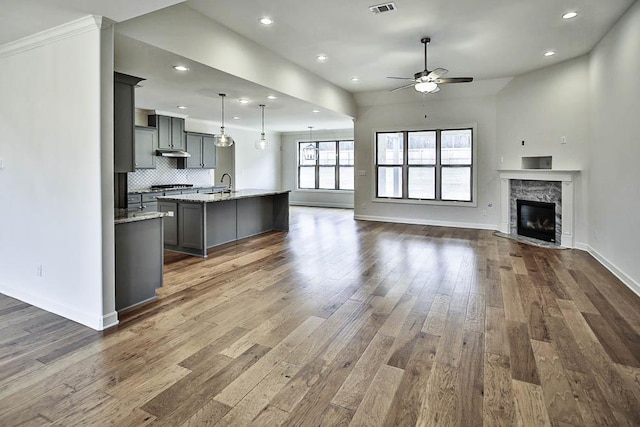 kitchen featuring gray cabinets, an island with sink, sink, hanging light fixtures, and light stone countertops