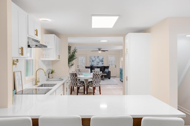 kitchen featuring a kitchen breakfast bar, kitchen peninsula, sink, and white cabinets