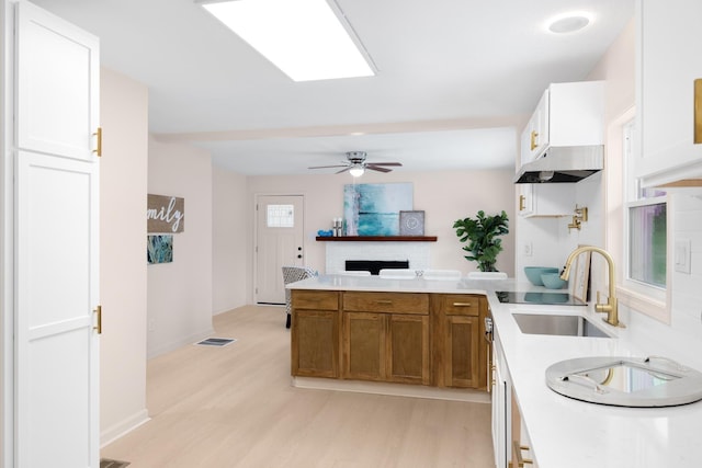 kitchen featuring sink, ceiling fan, white cabinetry, a fireplace, and light wood-type flooring