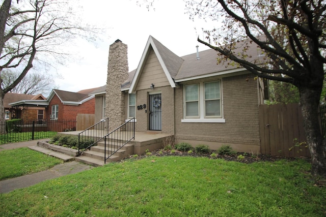 view of front of house featuring brick siding, a chimney, a front yard, and fence