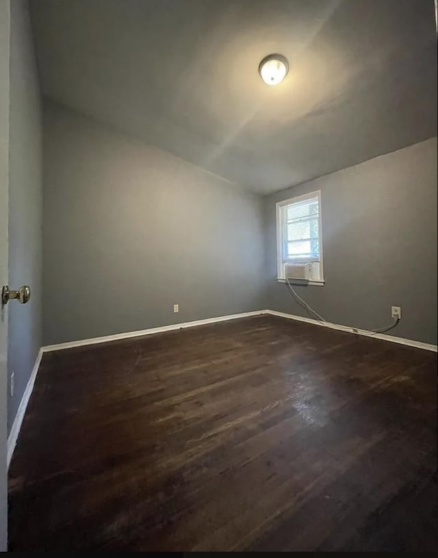 empty room featuring lofted ceiling, dark wood-style flooring, and baseboards