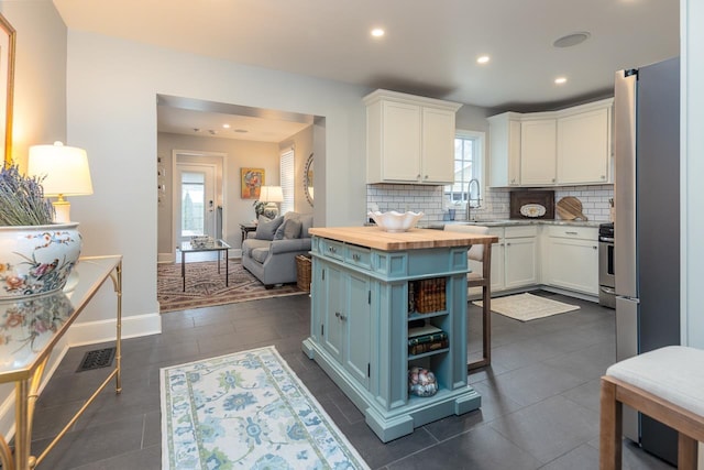 kitchen with tasteful backsplash, stainless steel stove, white cabinets, wood counters, and a kitchen island