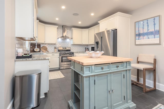 kitchen featuring white cabinetry, a kitchen island, wall chimney range hood, stainless steel appliances, and decorative backsplash