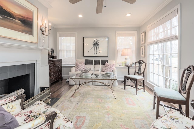 living area with a tile fireplace, ceiling fan, crown molding, and hardwood / wood-style floors