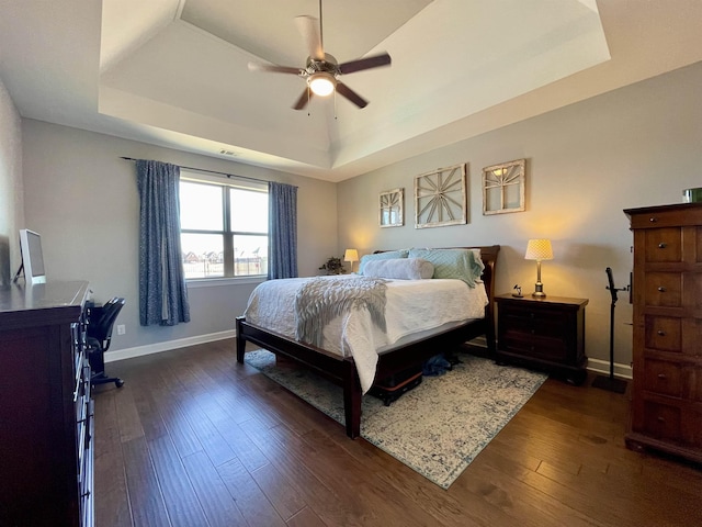 bedroom with dark wood-type flooring, ceiling fan, and a tray ceiling