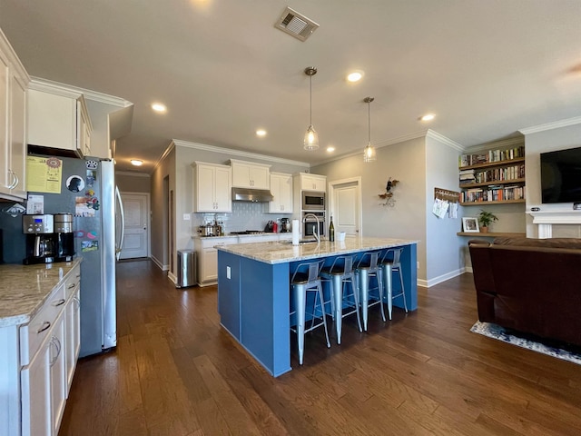 kitchen featuring white cabinetry, hanging light fixtures, a kitchen island with sink, stainless steel appliances, and a kitchen bar