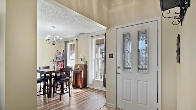 entrance foyer featuring a notable chandelier, crown molding, a textured ceiling, wood finished floors, and baseboards