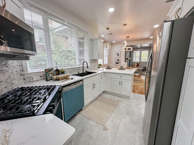 kitchen featuring hanging light fixtures, stainless steel appliances, sink, white cabinetry, and kitchen peninsula