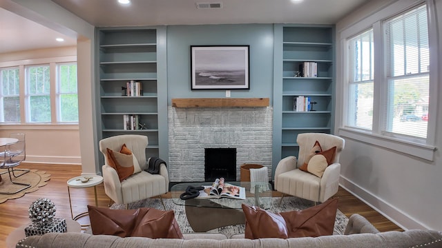 living room with built in features, a wealth of natural light, wood-type flooring, and a stone fireplace