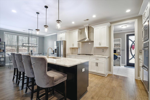 kitchen featuring appliances with stainless steel finishes, white cabinetry, pendant lighting, and wall chimney range hood