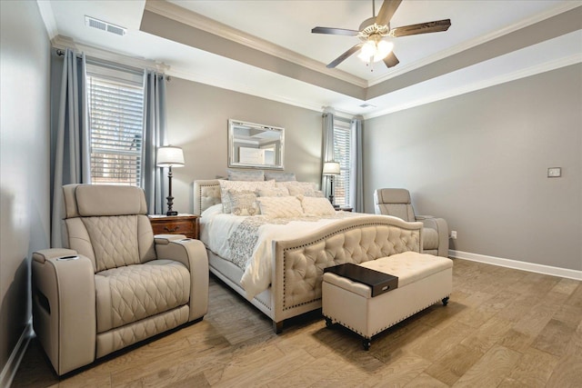 bedroom featuring ceiling fan, ornamental molding, light wood-type flooring, and a raised ceiling