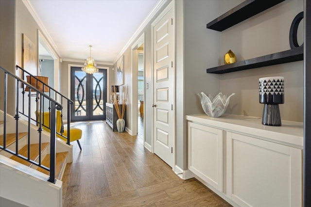 foyer entrance with light hardwood / wood-style flooring, french doors, a chandelier, and ornamental molding