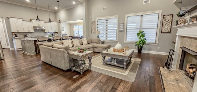 living room featuring an inviting chandelier, dark hardwood / wood-style floors, a tile fireplace, crown molding, and a high ceiling