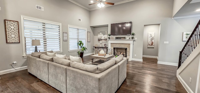 living room featuring a tiled fireplace, a high ceiling, ornamental molding, ceiling fan, and dark hardwood / wood-style floors