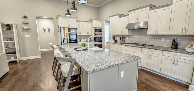 kitchen with a kitchen island with sink, stainless steel appliances, stone countertops, a breakfast bar area, and pendant lighting