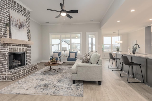 living room with sink, crown molding, a wealth of natural light, and light hardwood / wood-style floors