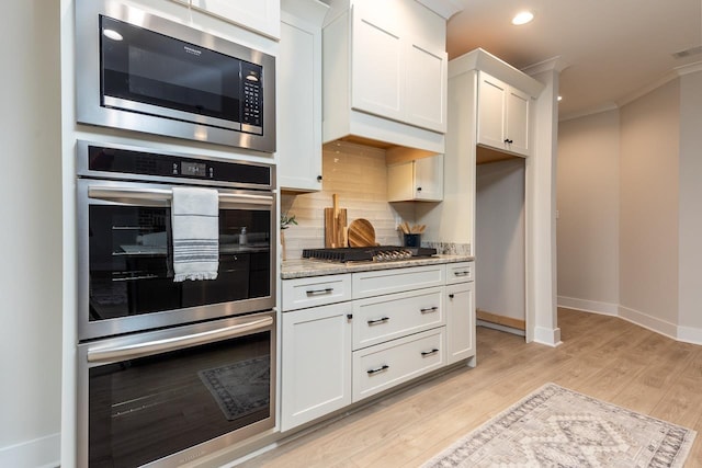 kitchen featuring appliances with stainless steel finishes, light stone counters, white cabinetry, crown molding, and decorative backsplash