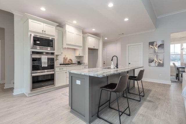 kitchen with appliances with stainless steel finishes, sink, a kitchen island with sink, and white cabinets