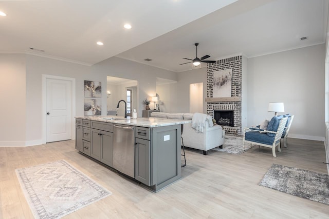 kitchen featuring a brick fireplace, sink, dishwasher, gray cabinetry, and a kitchen island with sink