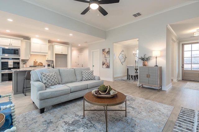 living room with ceiling fan with notable chandelier, crown molding, and light hardwood / wood-style flooring