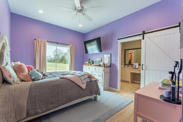 bedroom with ceiling fan, light hardwood / wood-style flooring, ensuite bath, and a barn door