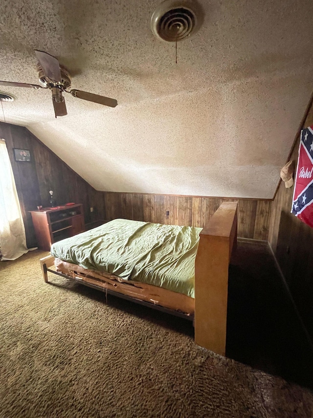 bedroom with lofted ceiling, carpet floors, wood walls, a textured ceiling, and ceiling fan