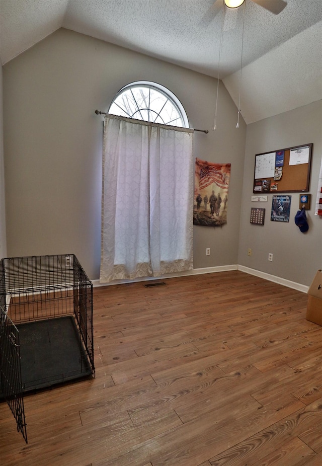 living area with ceiling fan, vaulted ceiling, a textured ceiling, and hardwood / wood-style flooring