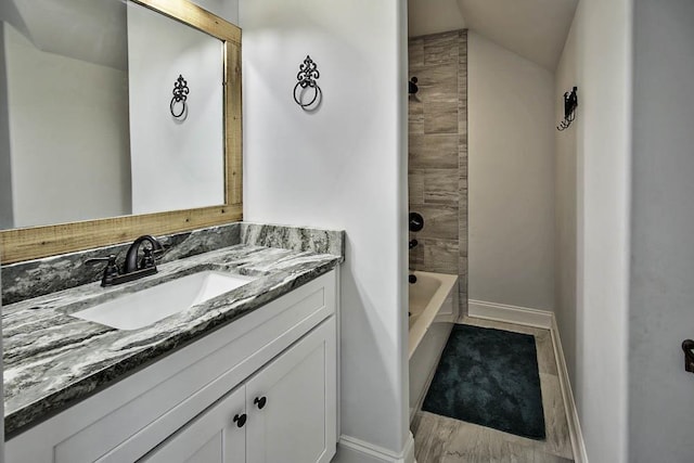 bathroom with vanity, vaulted ceiling, and tiled shower / bath