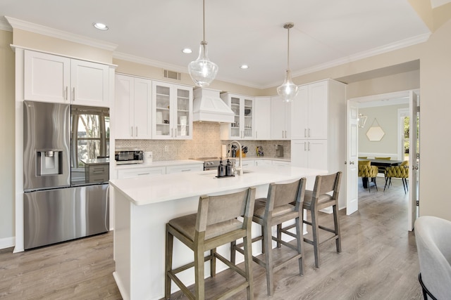 kitchen with an island with sink, white cabinetry, stainless steel refrigerator with ice dispenser, sink, and custom exhaust hood