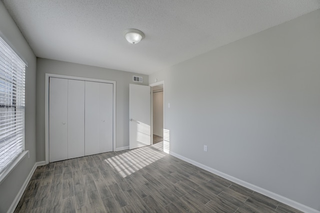 unfurnished bedroom featuring multiple windows, a closet, a textured ceiling, and dark hardwood / wood-style flooring