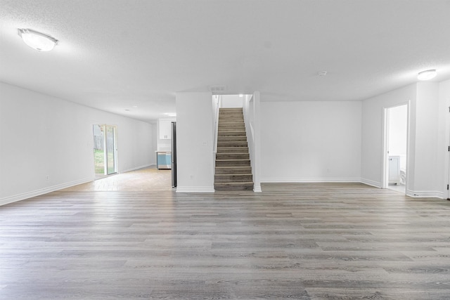 unfurnished living room featuring light wood-style flooring, baseboards, and stairway