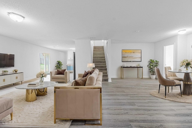 living room with light wood-style flooring, stairs, baseboards, and a textured ceiling