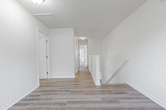 corridor featuring an upstairs landing, baseboards, attic access, light wood-style floors, and a textured ceiling