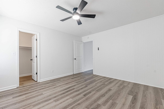 unfurnished bedroom featuring a ceiling fan, a textured ceiling, light wood-type flooring, a spacious closet, and a closet