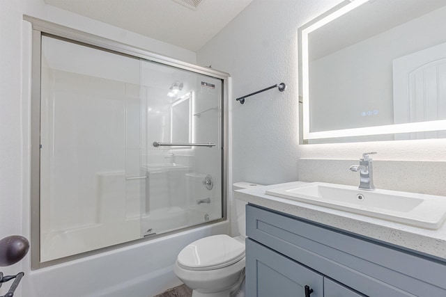 bathroom featuring vanity, shower / bath combination with glass door, toilet, and a textured wall