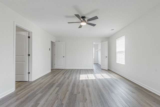 unfurnished bedroom featuring visible vents, a walk in closet, baseboards, light wood-type flooring, and ceiling fan