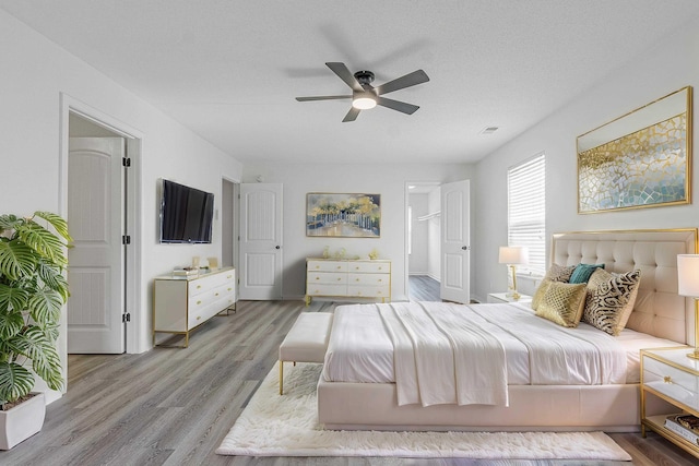 bedroom featuring light wood-type flooring, visible vents, a ceiling fan, and a textured ceiling