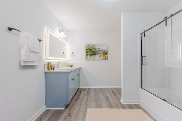 full bath with baseboards, vanity, bath / shower combo with glass door, and wood finished floors