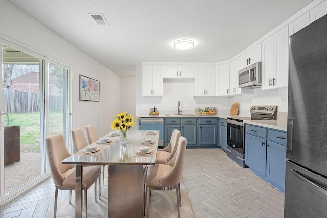 kitchen with visible vents, light countertops, white cabinetry, stainless steel appliances, and blue cabinetry