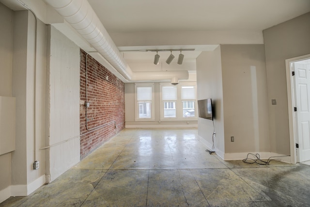 interior space with baseboards, brick wall, and track lighting