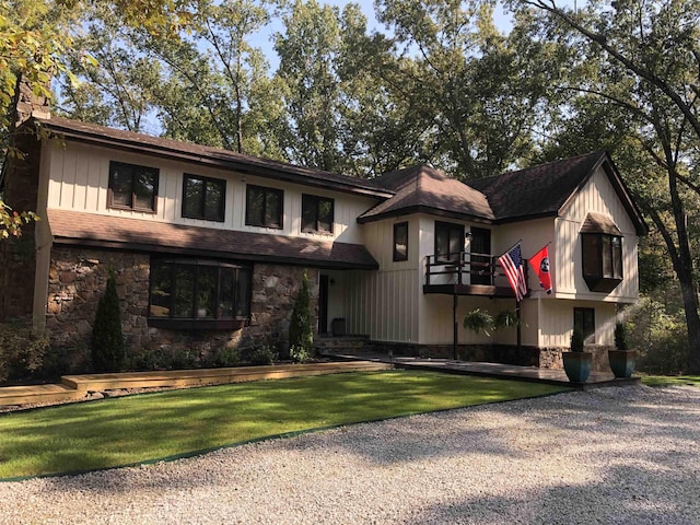 view of front of home with a front lawn, stone siding, gravel driveway, board and batten siding, and a balcony