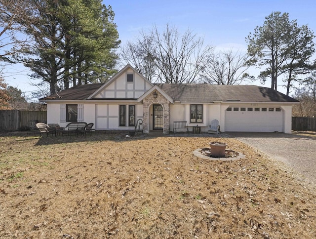 view of front of house featuring gravel driveway, fence, a garage, stone siding, and a front lawn