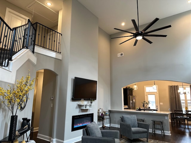 living area with arched walkways, a high ceiling, a glass covered fireplace, and visible vents