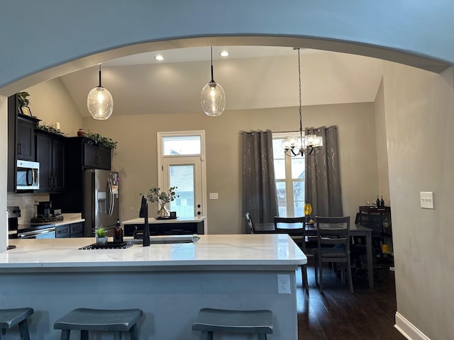 kitchen featuring lofted ceiling, a peninsula, appliances with stainless steel finishes, and decorative light fixtures