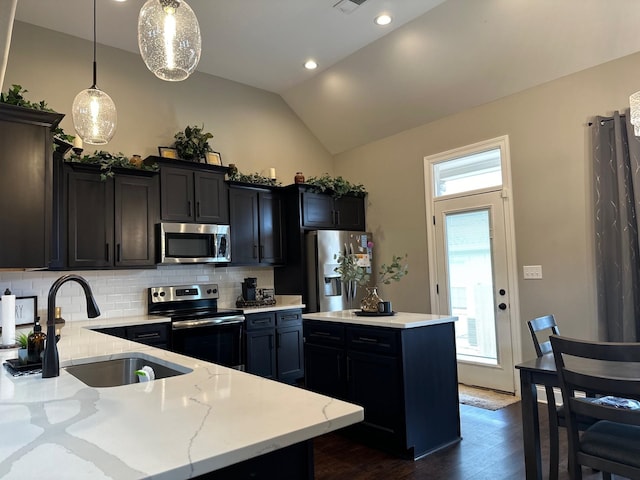 kitchen featuring light stone counters, a sink, appliances with stainless steel finishes, a center island, and decorative light fixtures