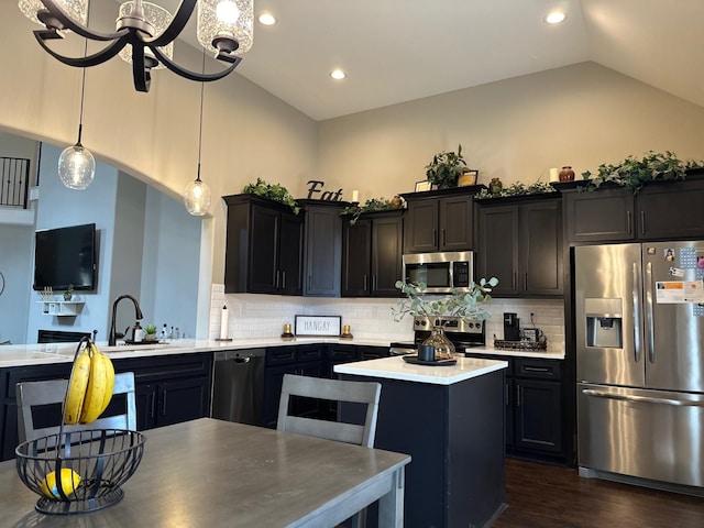 kitchen with lofted ceiling, stainless steel appliances, light countertops, a center island, and pendant lighting