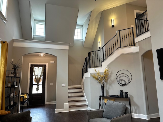 foyer with arched walkways, a high ceiling, dark wood-style flooring, and baseboards