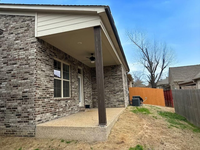 view of side of property featuring central AC unit, a ceiling fan, a patio, fence, and brick siding